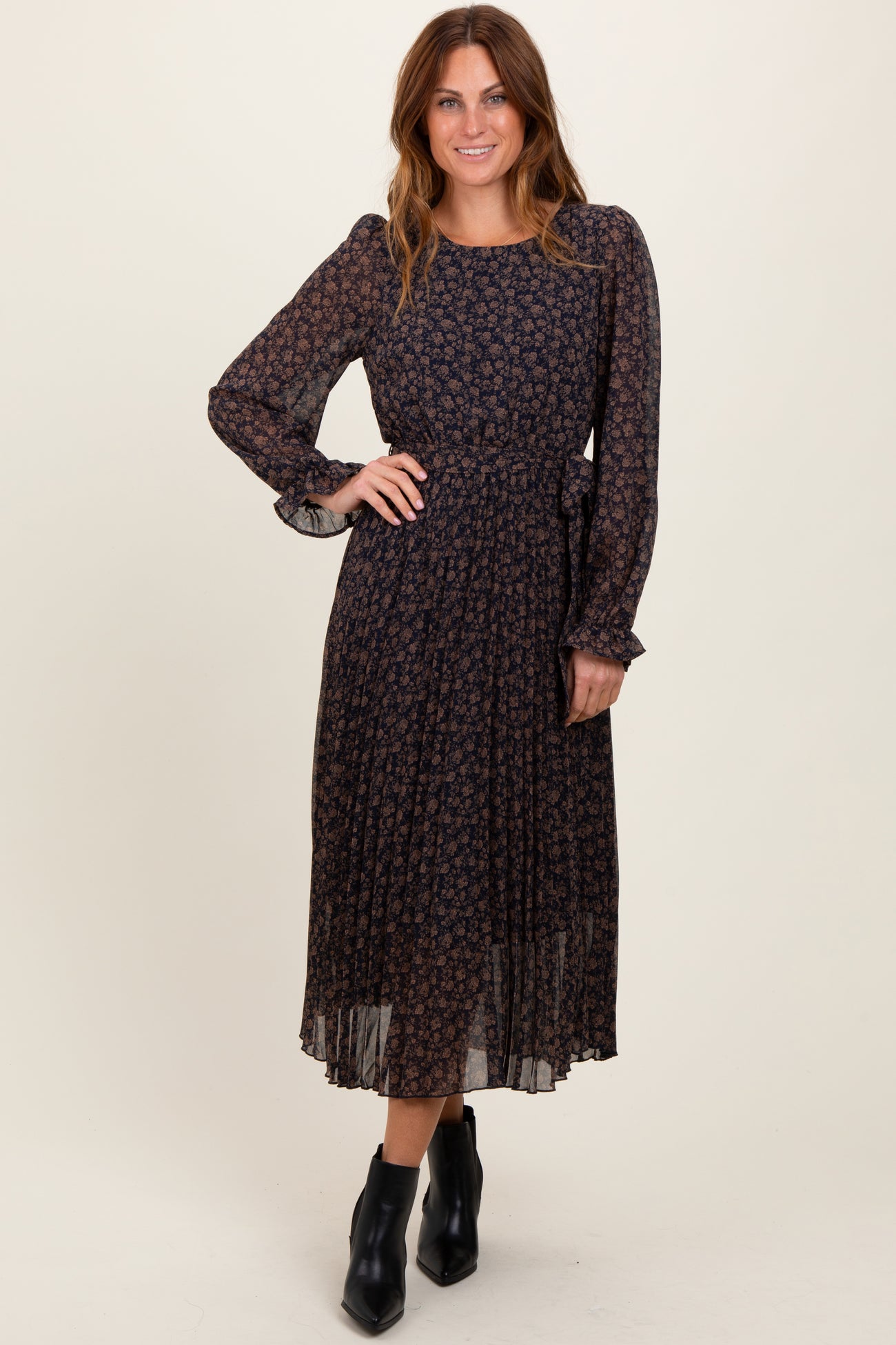 woman wearing a dark floral long sleeve pleated dress with a cinched waist and black ankle boots