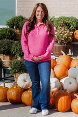 woman wearing a pink ribbed maternity sweater and blue jeans, holding her baby bump in front of pumpkins
