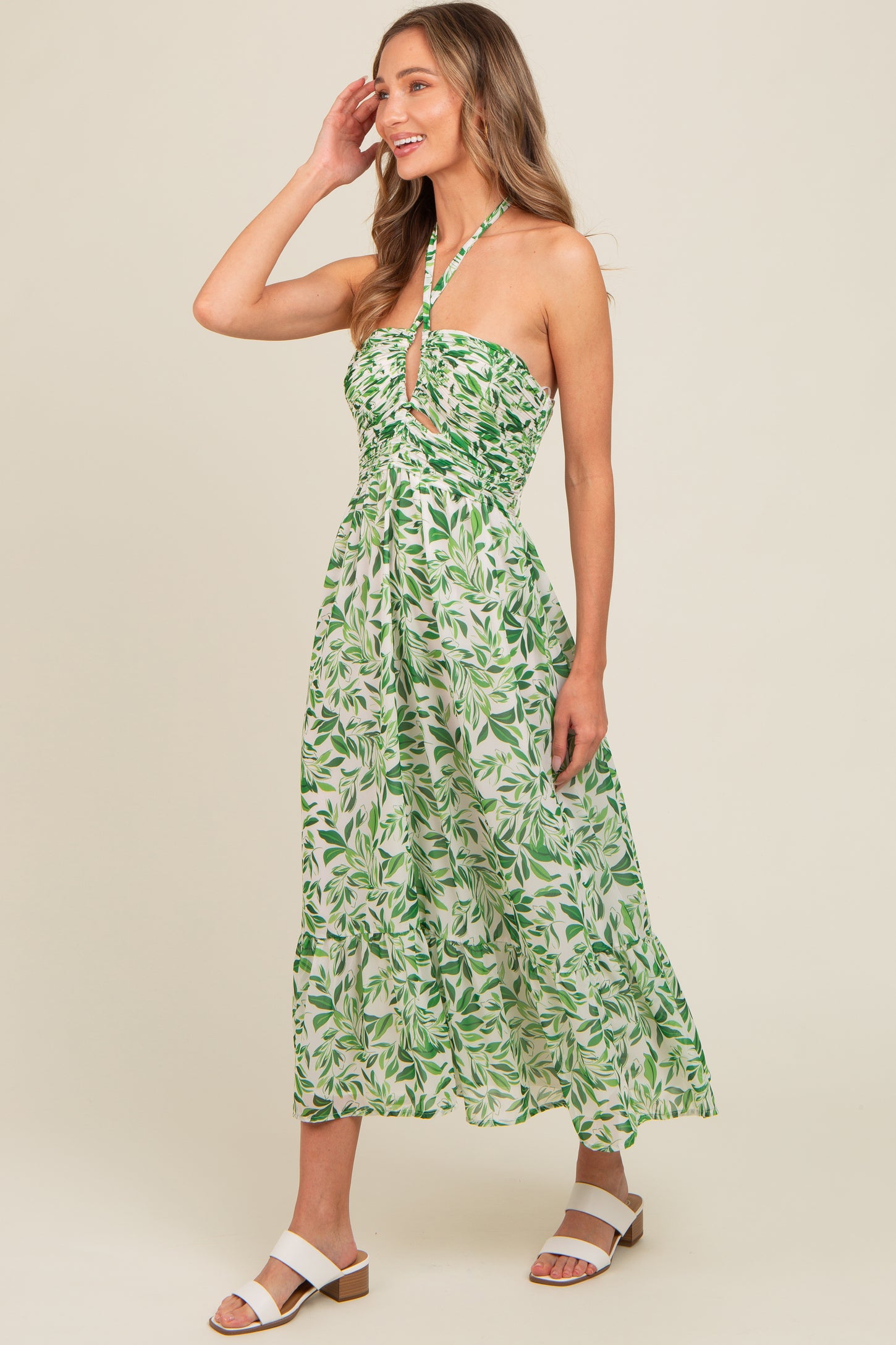 woman wearing a green and white floral maxi dress with a halter neck and ruched bodice, smiling and posing sideways