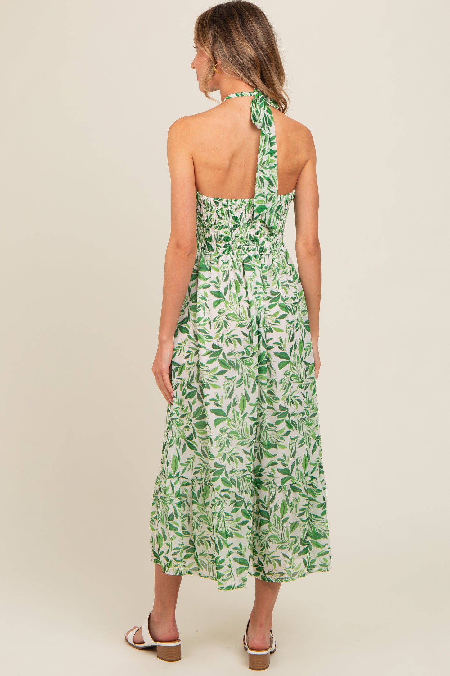 woman wearing a backless green leaf print maxi dress with a halter neck and smocked bodice