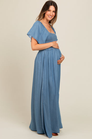 woman wearing a light blue maternity maxi dress with smocked bodice and flutter sleeves, gently cradling her baby bump