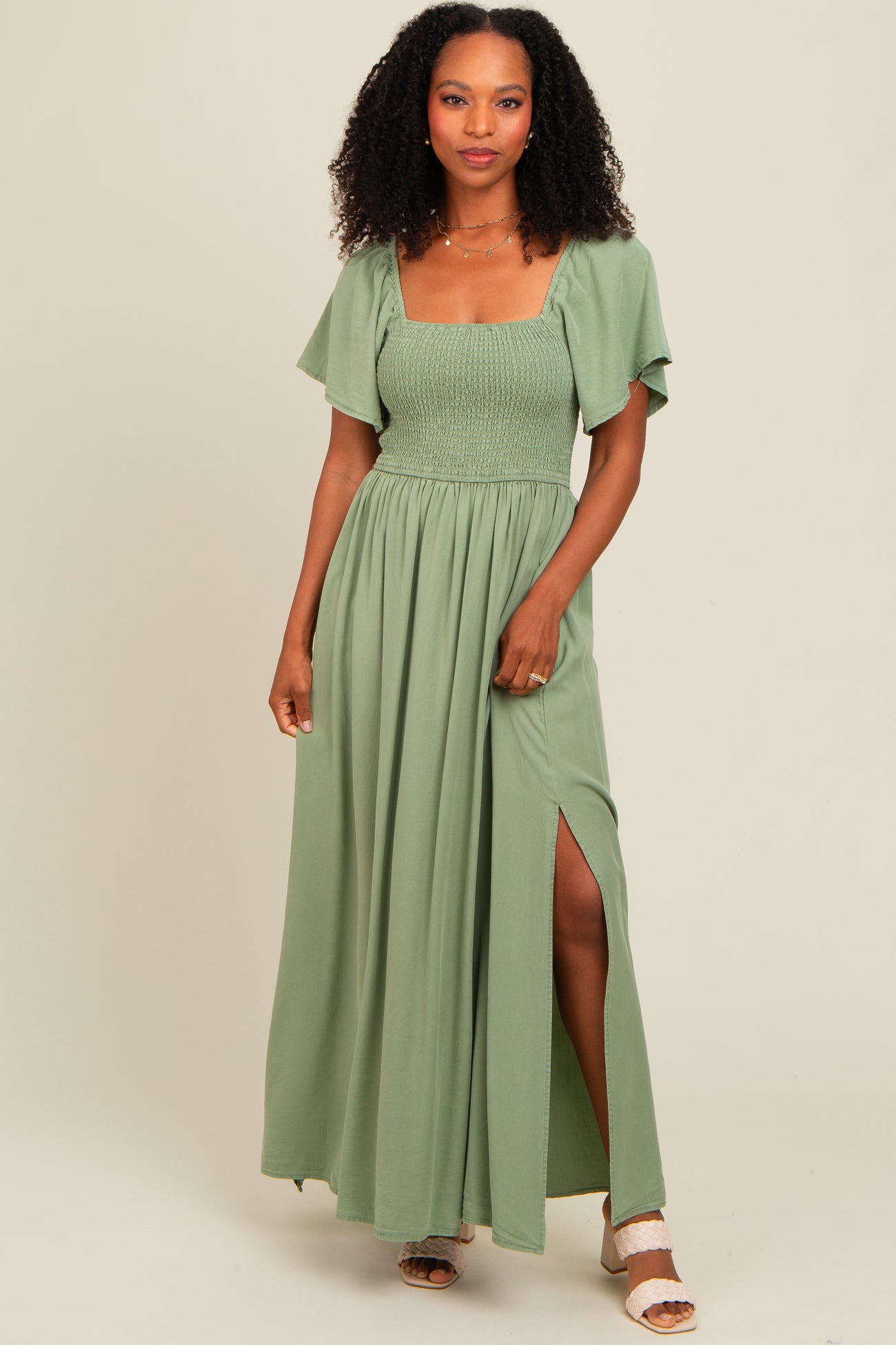 woman wearing a green maxi dress with smocked bodice and flutter sleeves, featuring a thigh-high slit