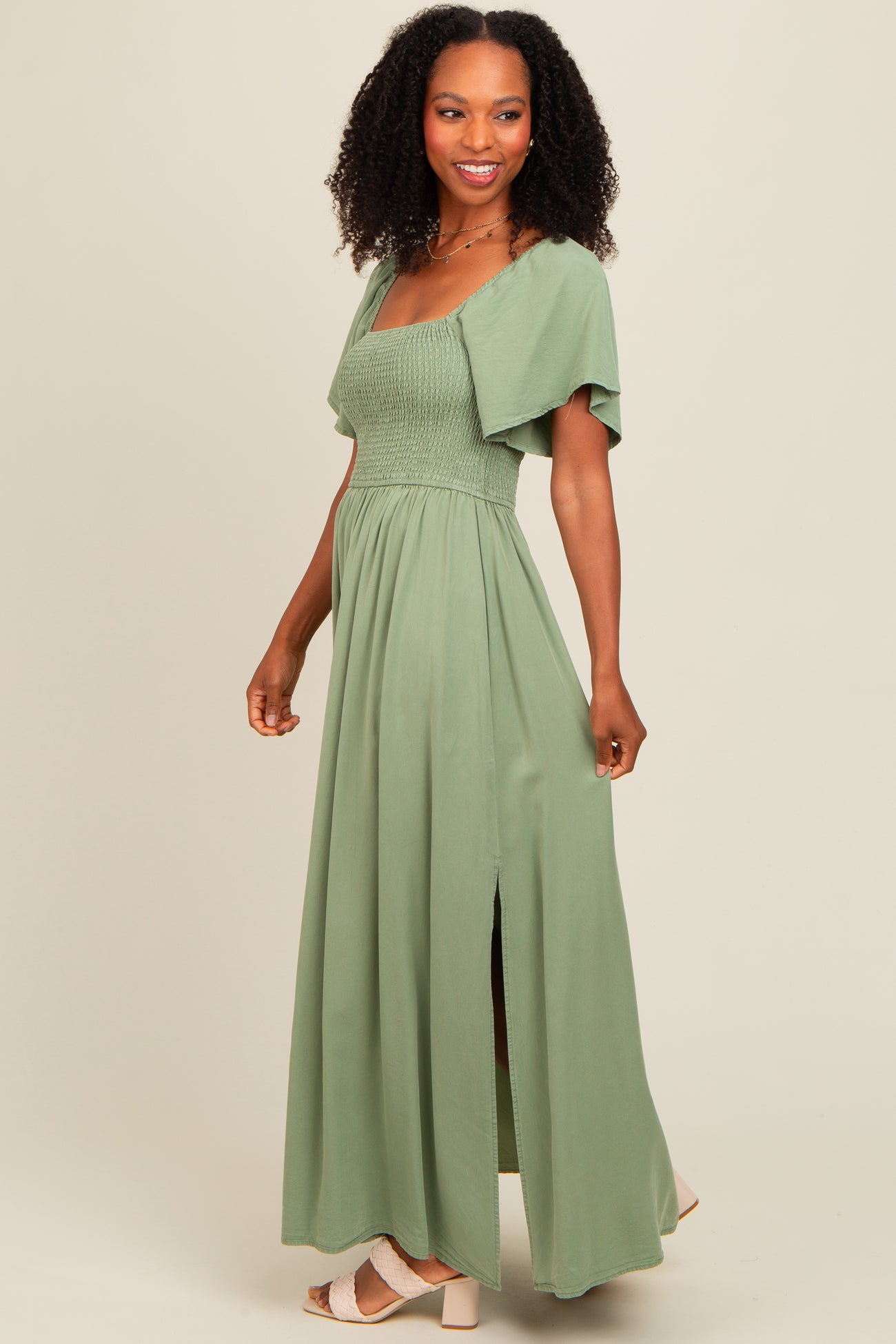 woman wearing a light green maxi dress with a smocked bodice and short sleeves, featuring a side slit
