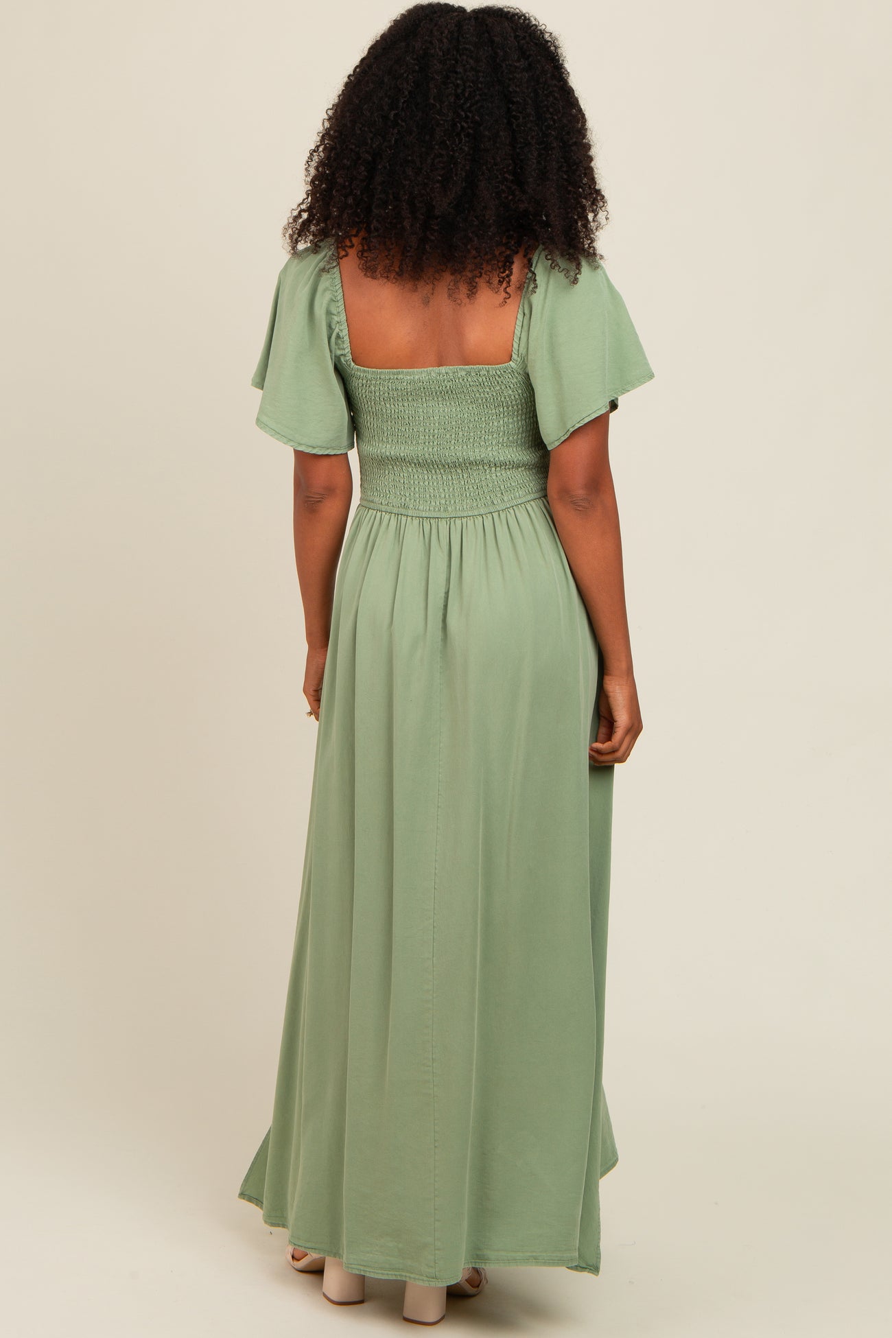 woman wearing a back view of a light green smocked maxi dress with flutter sleeves and a flowing skirt