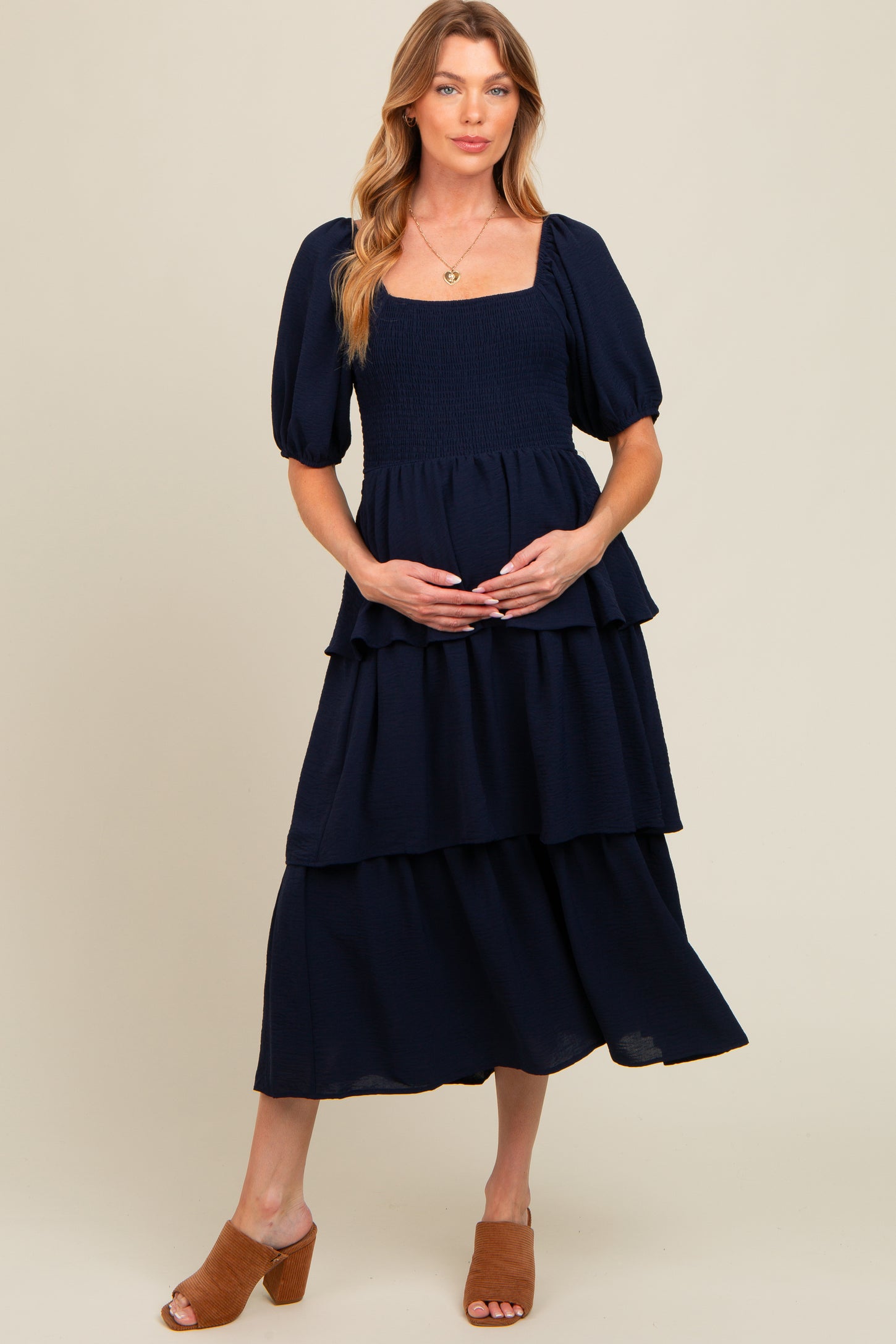 woman wearing a navy blue maternity tiered maxi dress with puff sleeves and holding her baby bump
