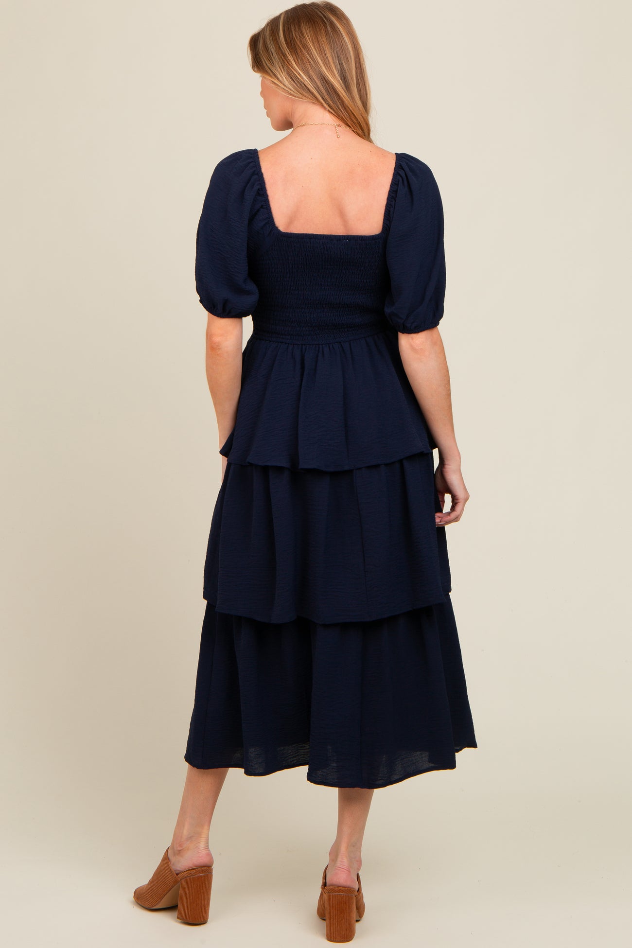 woman wearing a navy blue maternity tiered dress with puff sleeves and a smocked bodice, viewed from the back