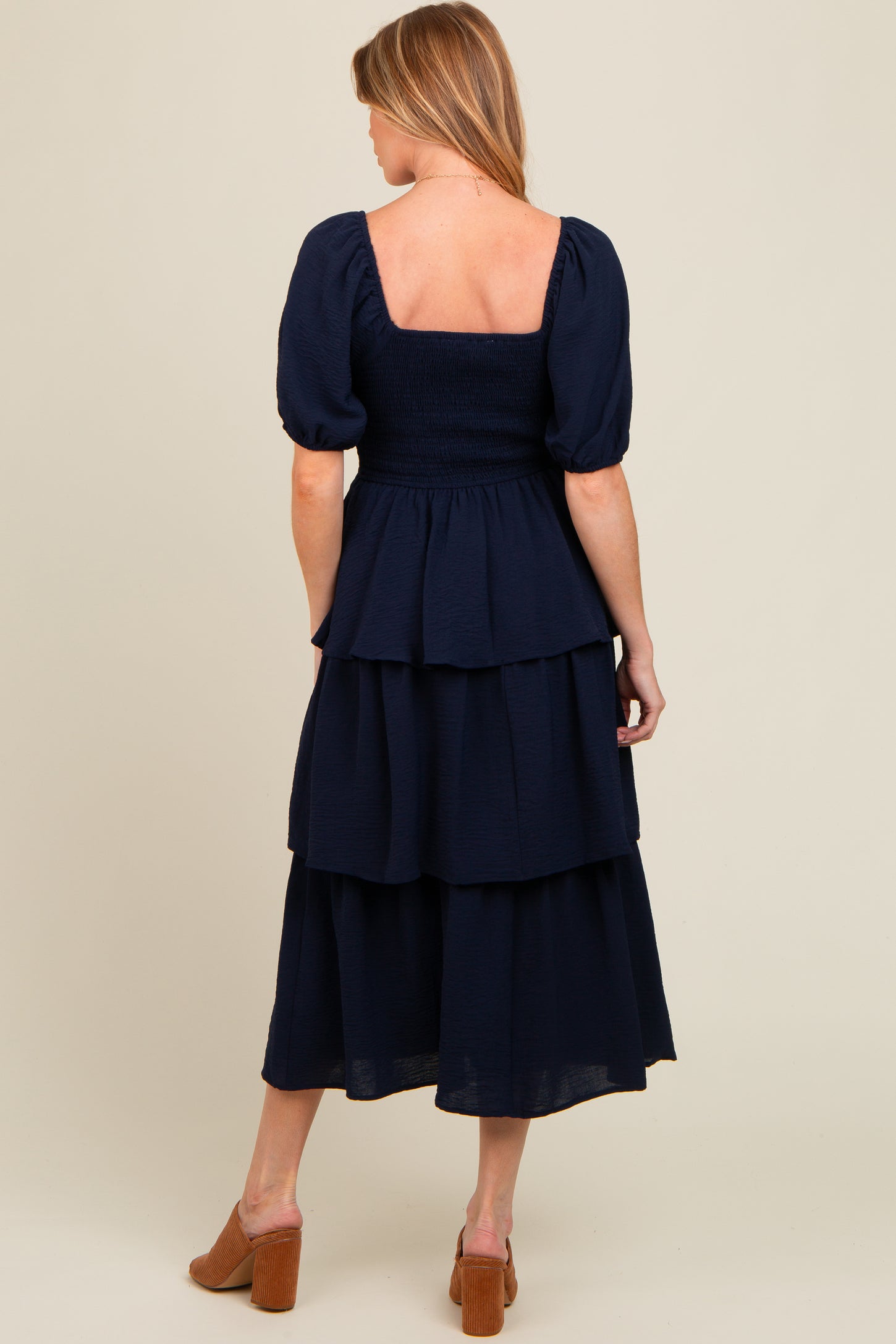 woman wearing a navy blue maternity tiered dress with puff sleeves and a smocked bodice, viewed from the back