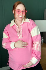 woman wearing a pink colorblock maternity sweatshirt with striped details and holding her baby bump