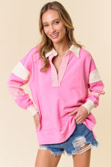woman wearing a pink long sleeve pullover with striped collar and sleeves, paired with distressed denim shorts
