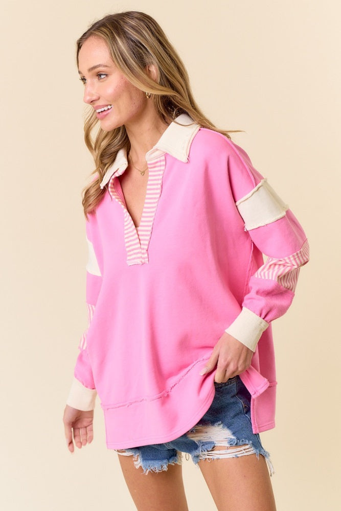 woman wearing a pink pullover sweatshirt with striped sleeves and collar, styled with distressed denim shorts