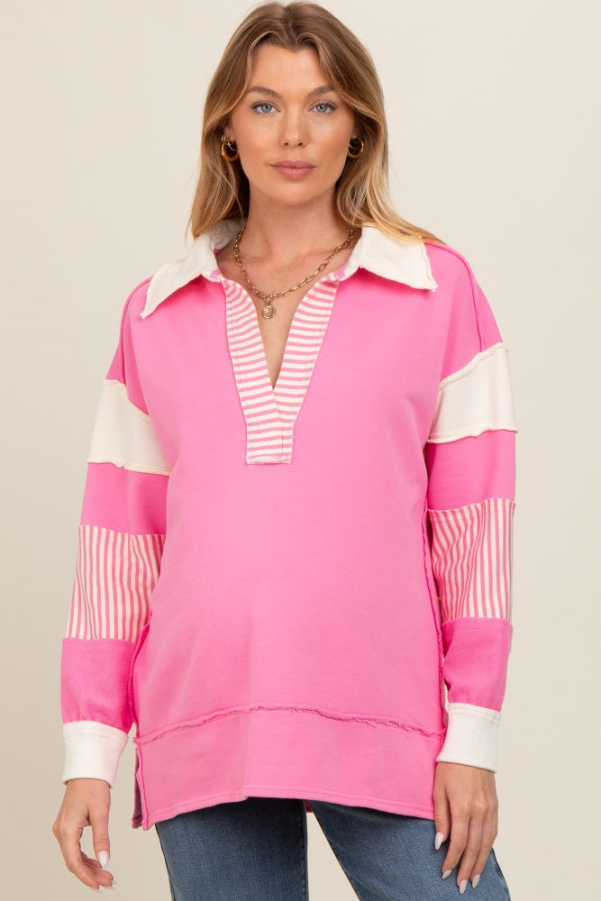 woman wearing a pink maternity pullover with a collared neckline and striped sleeve details, showcasing her baby bump
