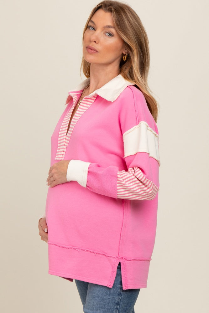 woman wearing a pink maternity pullover with striped sleeves and a collared neckline, holding her baby bump