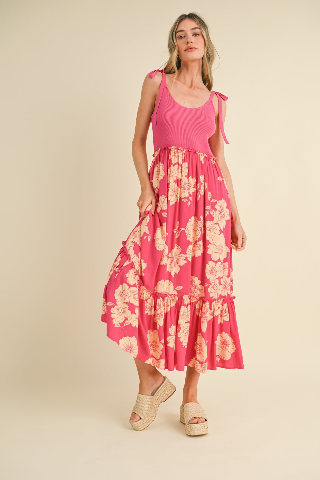 woman wearing a pink floral maxi dress with a fitted bodice and ruffled skirt, styled with a braided hairstyle and sandals
