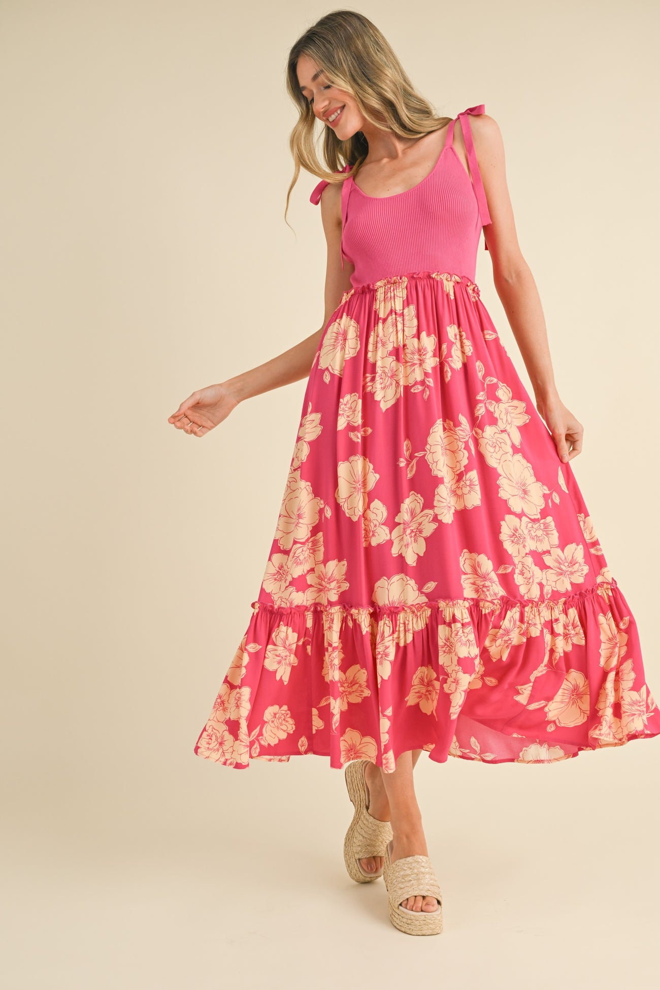 woman wearing a pink floral maxi dress with spaghetti straps and ruffled hem, posing joyfully
