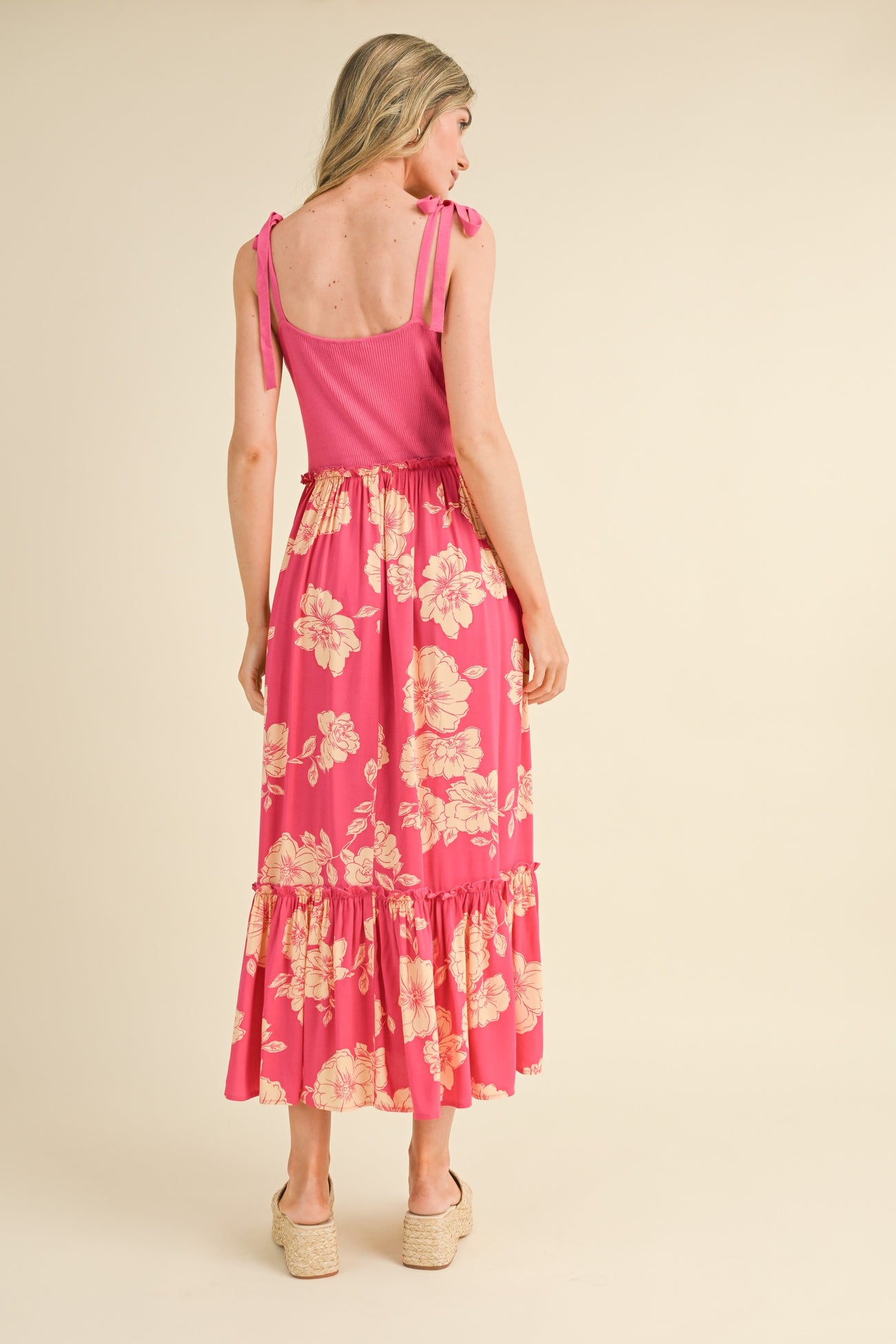 woman wearing a pink floral maxi dress with ruffle details and adjustable straps, view from the back