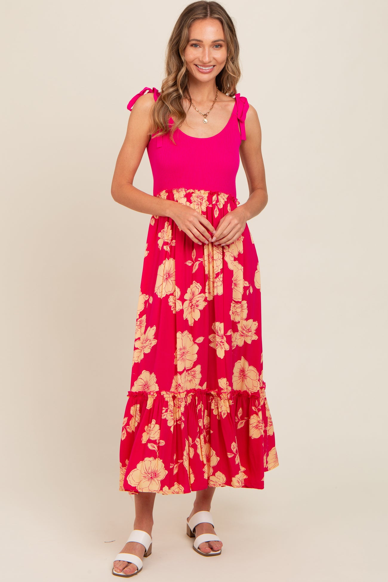 woman wearing a bright pink floral maxi dress with tie shoulder straps and a ruffled hem