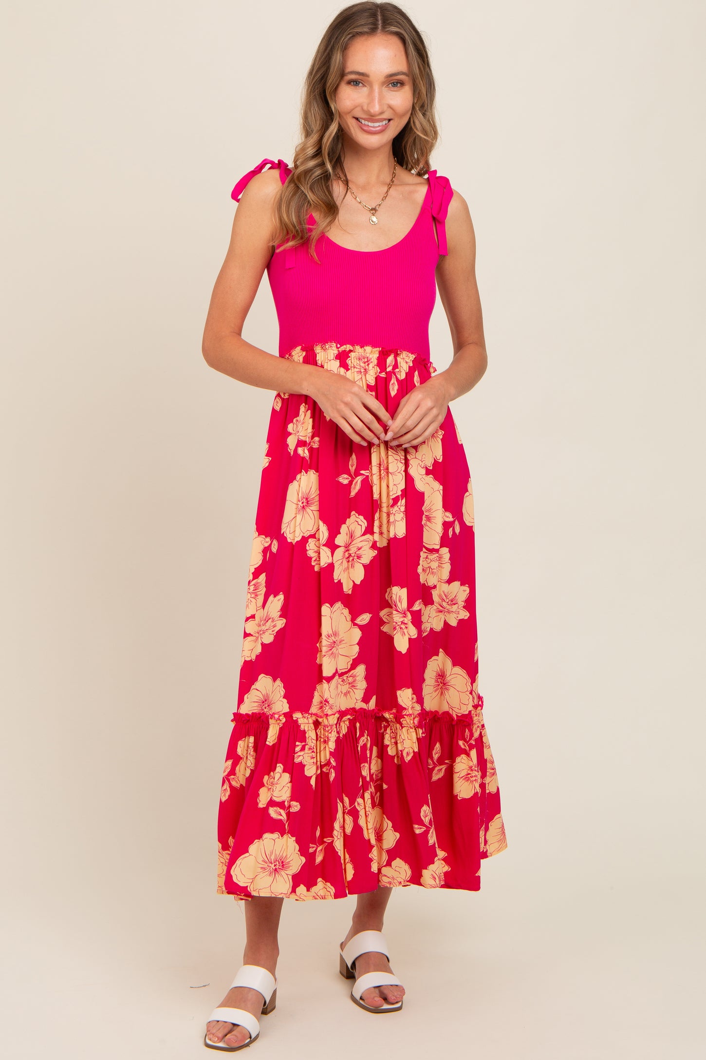 woman wearing a bright pink floral maxi dress with tie shoulder straps and a ruffled hem