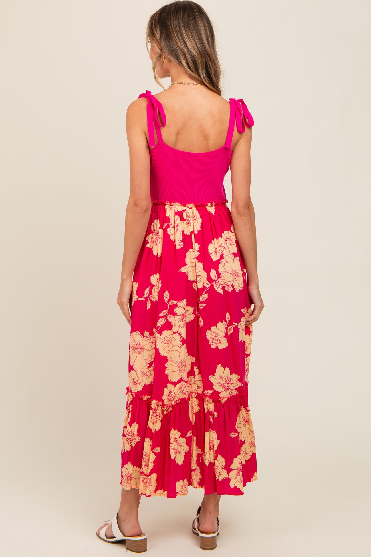 woman wearing a pink floral maxi dress with tie straps and a tiered skirt, viewed from the back