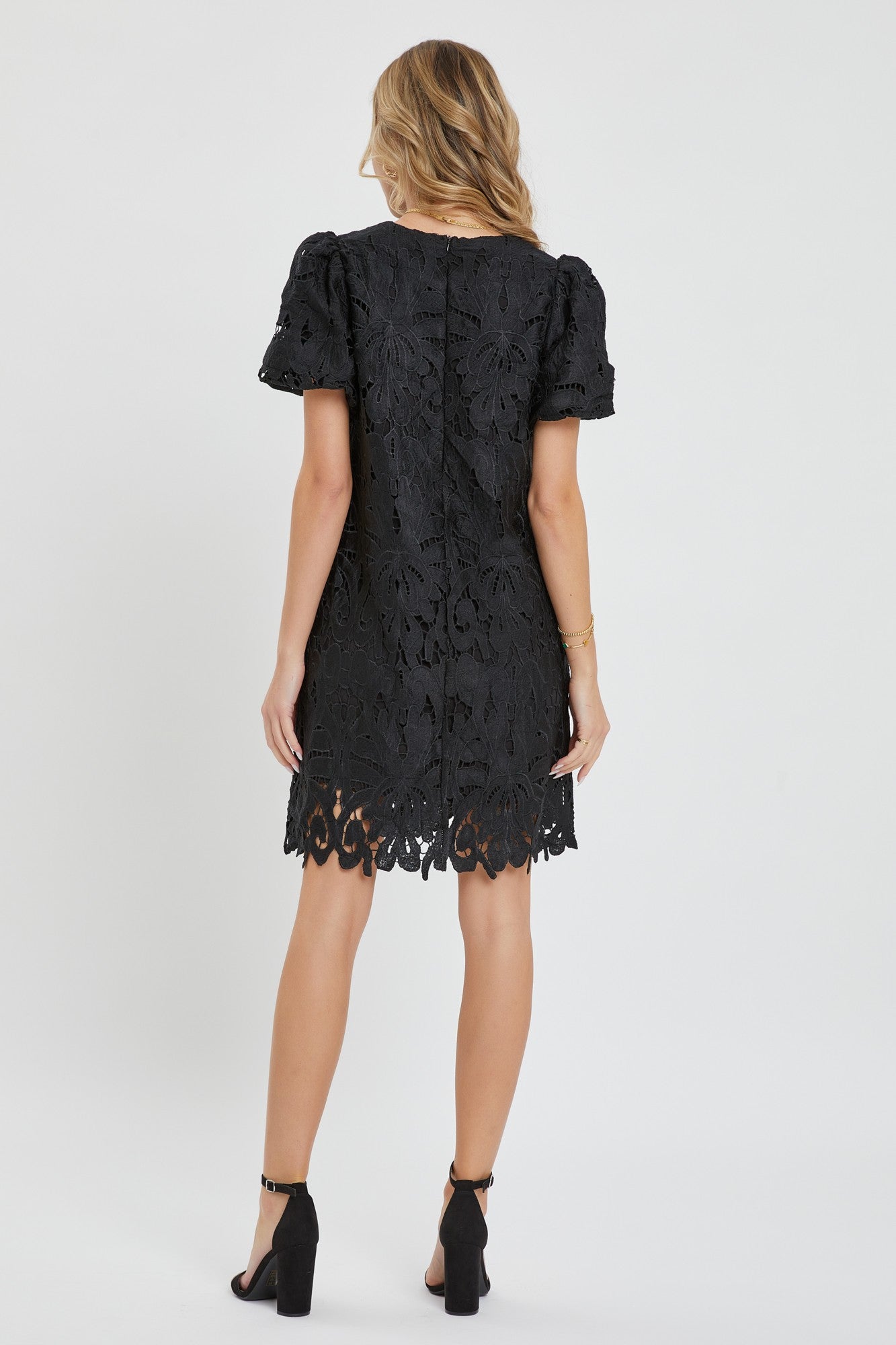 woman wearing a black lace short sleeve dress with a scalloped hem and back zipper detail