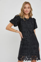 woman wearing a black short sleeve lace dress with floral patterns and a scalloped hemline