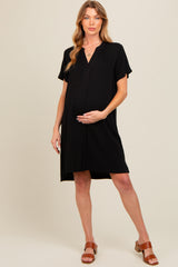 woman wearing a black short sleeve maternity dress, smiling and holding her baby bump