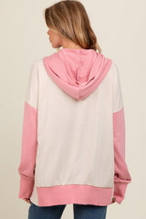 woman wearing a color-blocked pink and cream maternity hoodie with a hood, showing the back view