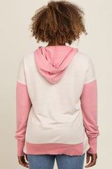 woman wearing a light pink and cream colorblock hoodie with a front pocket and a hood, seen from the back