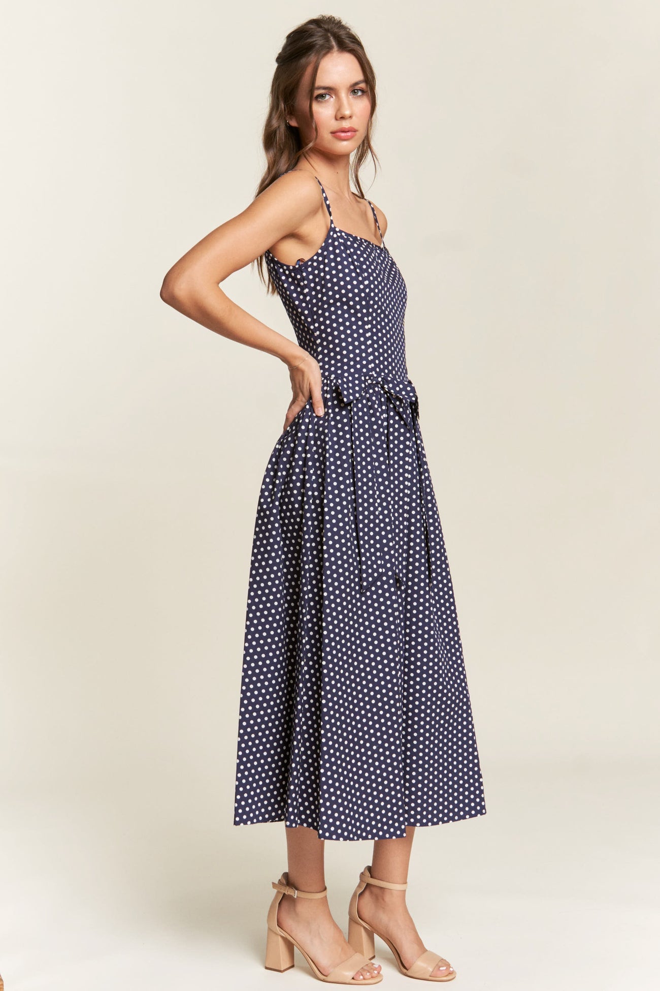 woman wearing a navy blue polka dot midi dress with spaghetti straps and a tied waist detail