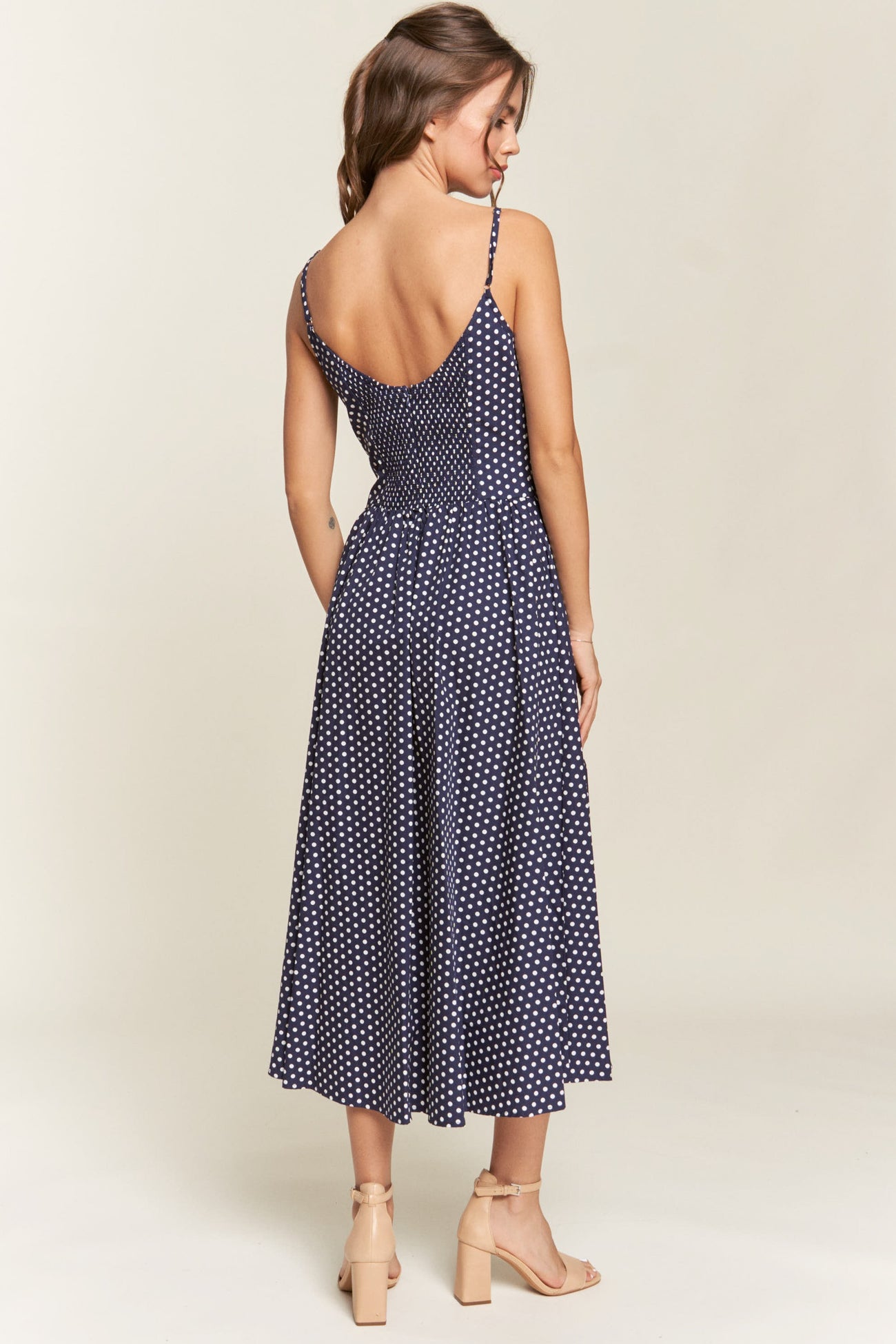 woman wearing a navy blue polka dot midi dress with adjustable straps and a fitted bodice viewed from the back