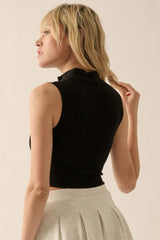 woman wearing a black sleeveless cropped top with a ruffled neckline and styled hair, posed from the side