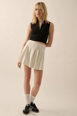 woman wearing a black sleeveless top and a light gray pleated mini skirt with black sneakers and white crew socks