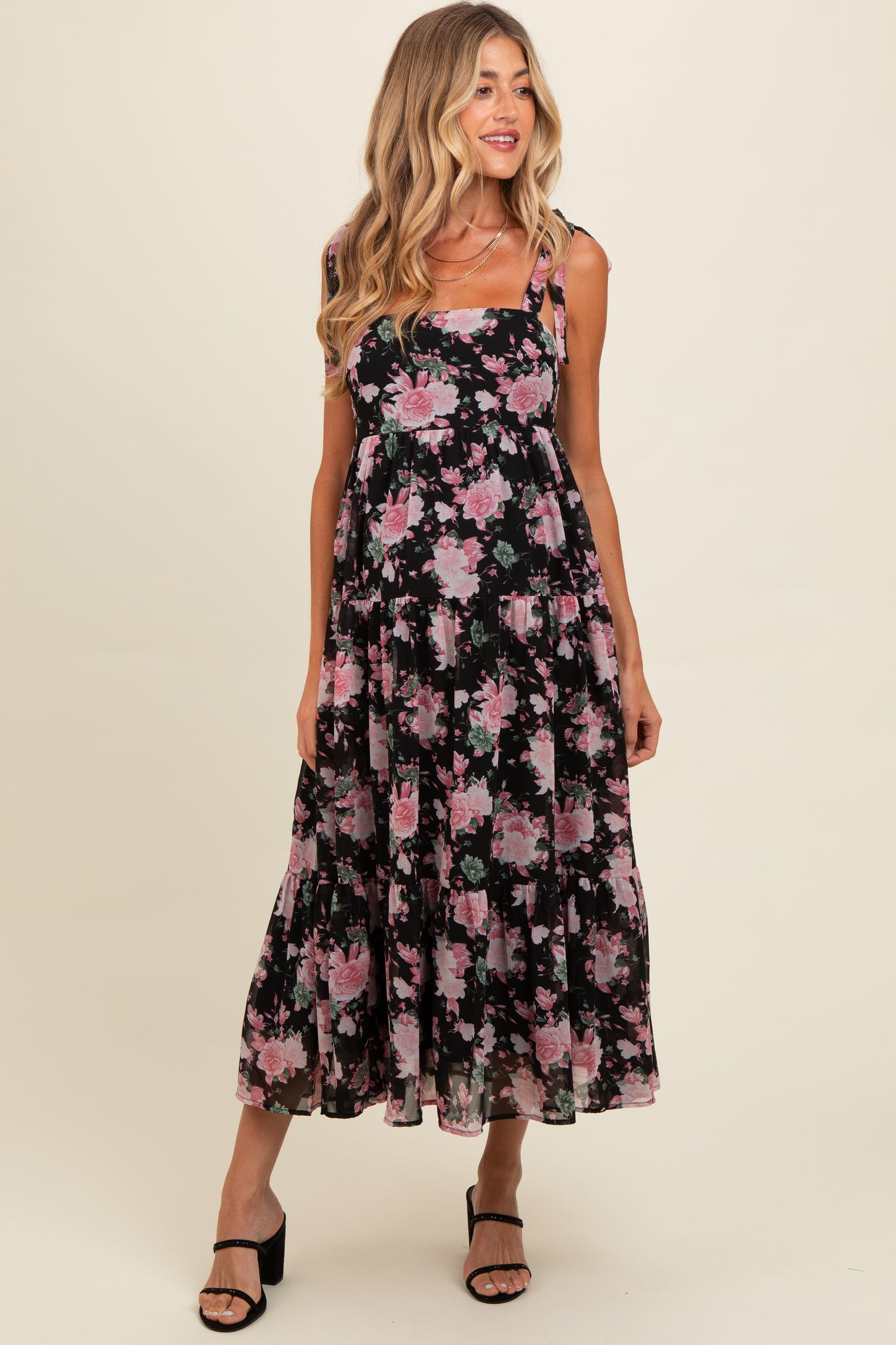 woman wearing a black floral maternity maxi dress with tiered details and spaghetti straps, showcasing her baby bump