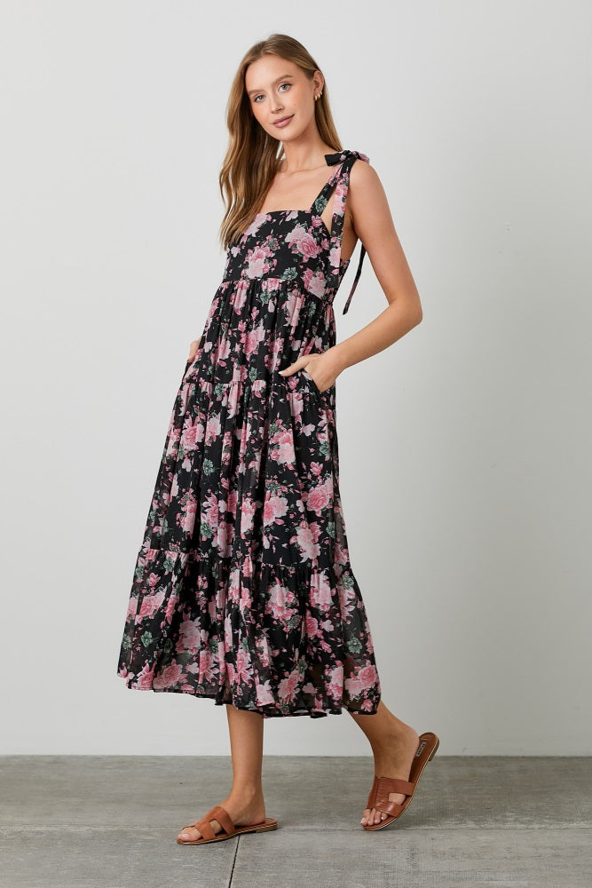 woman wearing a black floral maxi dress with adjustable straps and pockets, styled with brown sandals