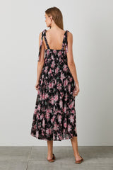 woman wearing a black floral maxi dress with pink roses and tie straps, viewed from the back