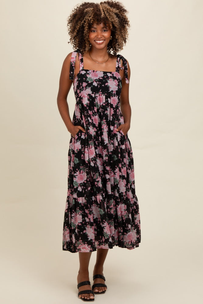 woman wearing a black floral midi dress with adjustable shoulder straps and pockets