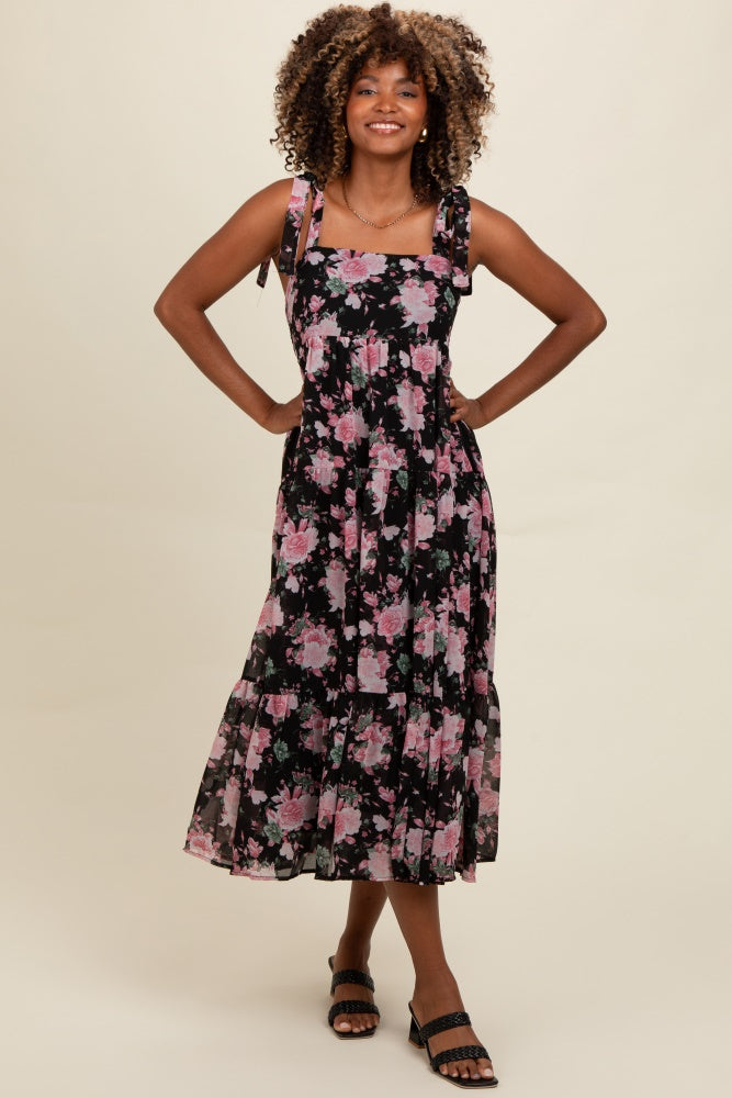 woman wearing a black floral midi dress with pink flowers and tie straps, standing and smiling