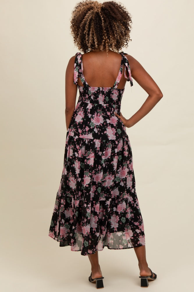 woman wearing a black floral maxi dress with adjustable tie straps and a tiered skirt view from the back