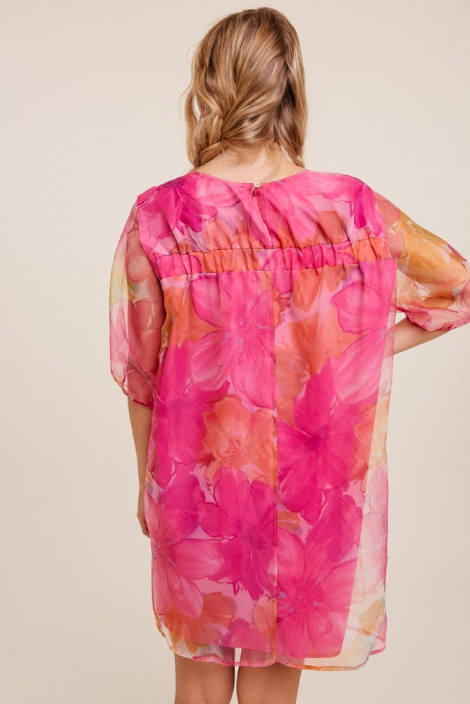 woman wearing a sheer pink floral dress with loose sleeves and a gathered waist from the back