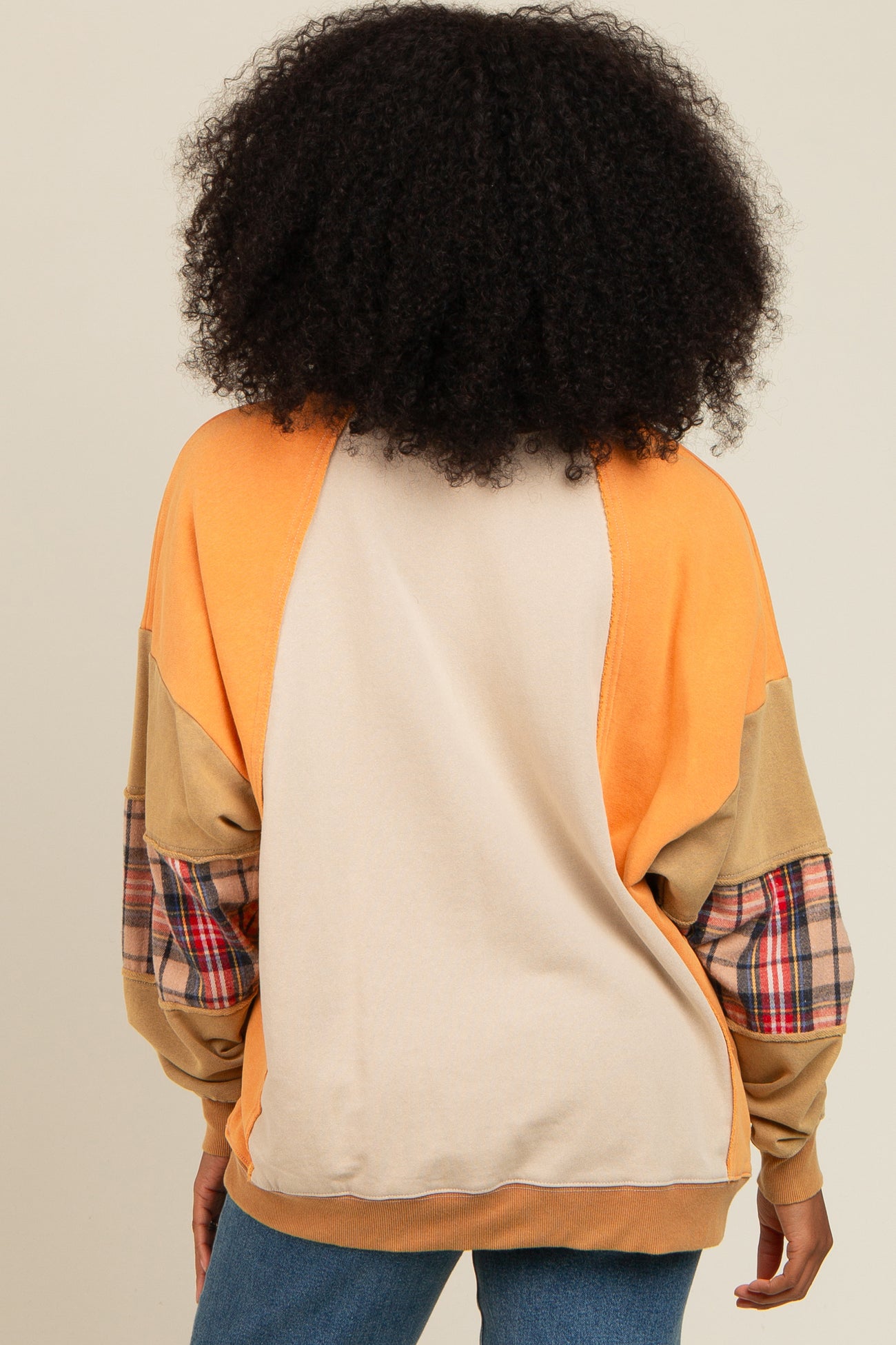 woman wearing an orange and beige color block sweater with plaid details on the sleeves, viewed from the back