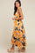 woman wearing an orange and white maxi dress with abstract leaf patterns and a tied detail at the shoulder