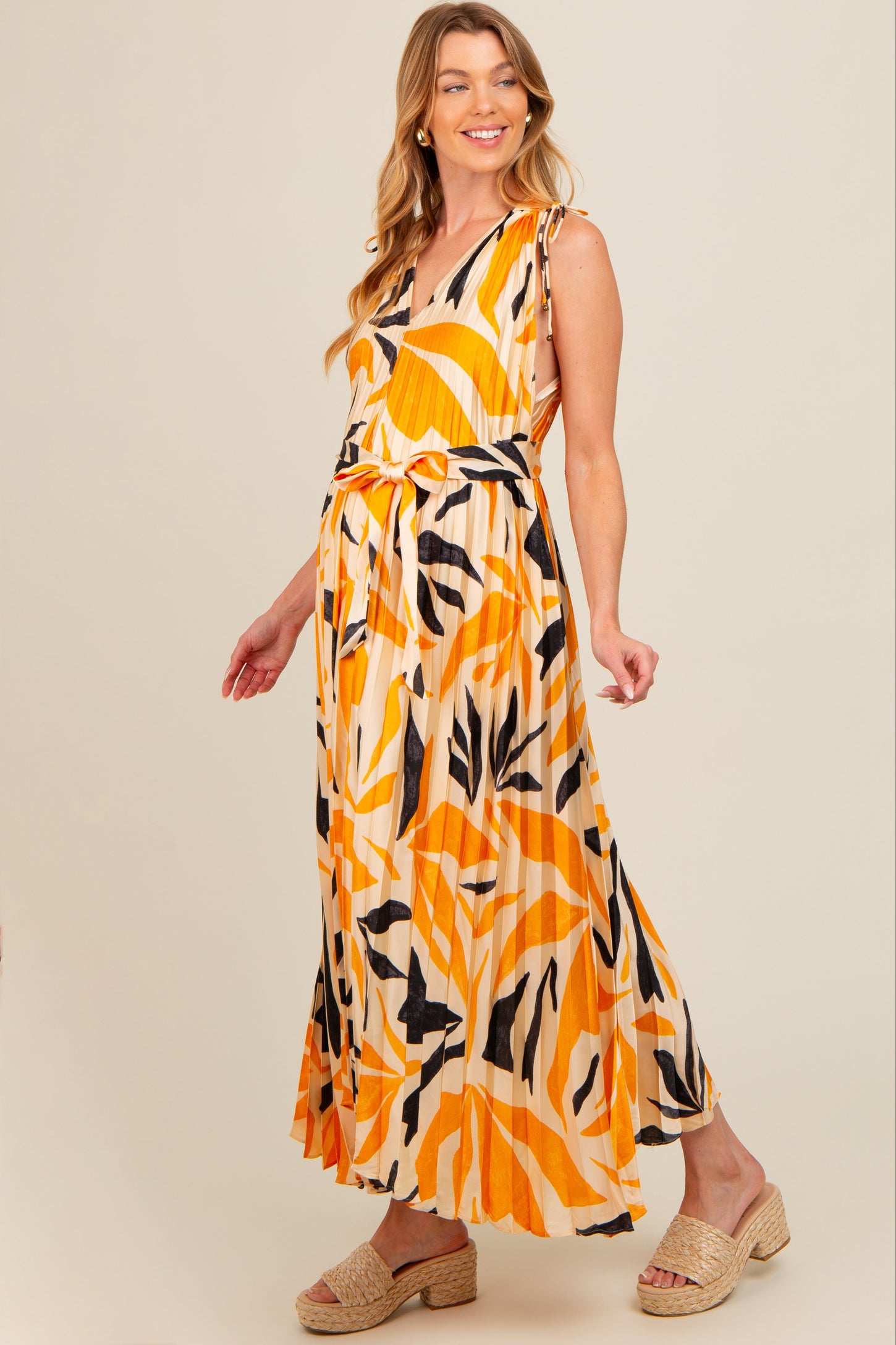 woman wearing a yellow and black abstract print maternity maxi dress with a tie waist and flowing skirt, showing her baby bump