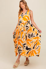 woman wearing a vibrant orange and black floral print maternity maxi dress with tie straps and a belted waist