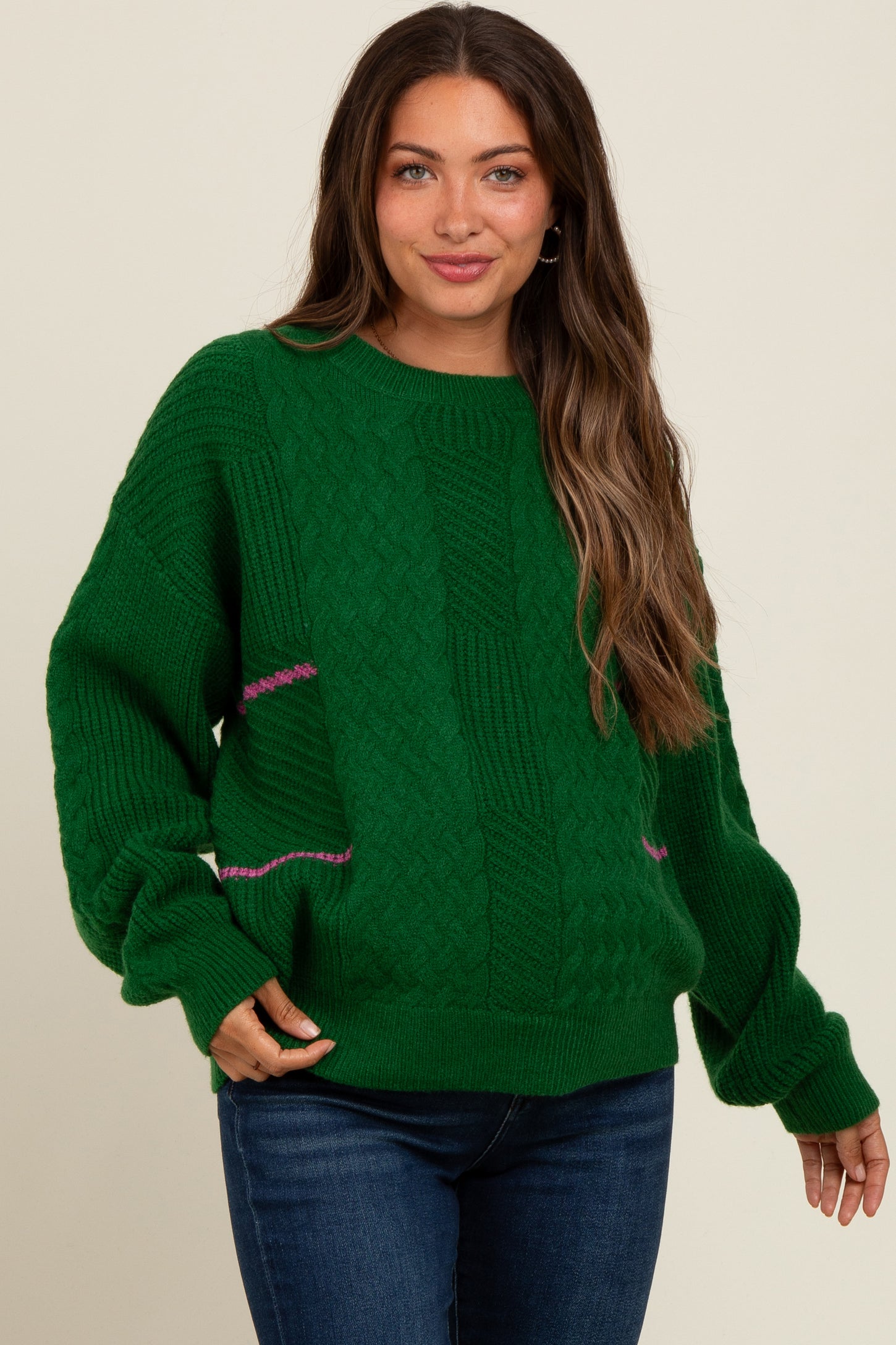 woman wearing a green knitted maternity sweater with cable knit design and relaxed fit, paired with blue jeans
