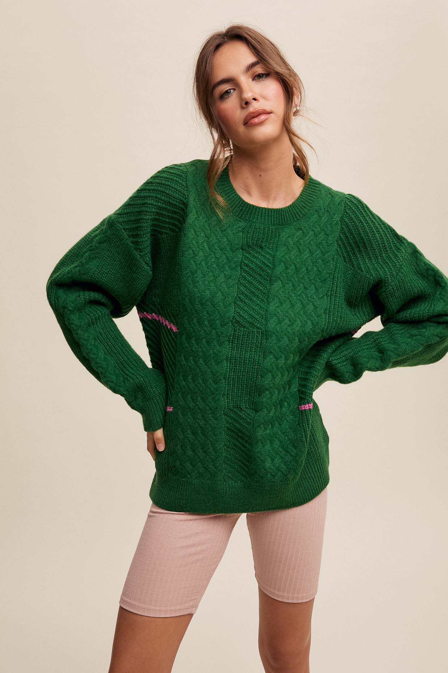 woman wearing a green cable knit sweater with puff sleeves and pink accents paired with light pink bike shorts