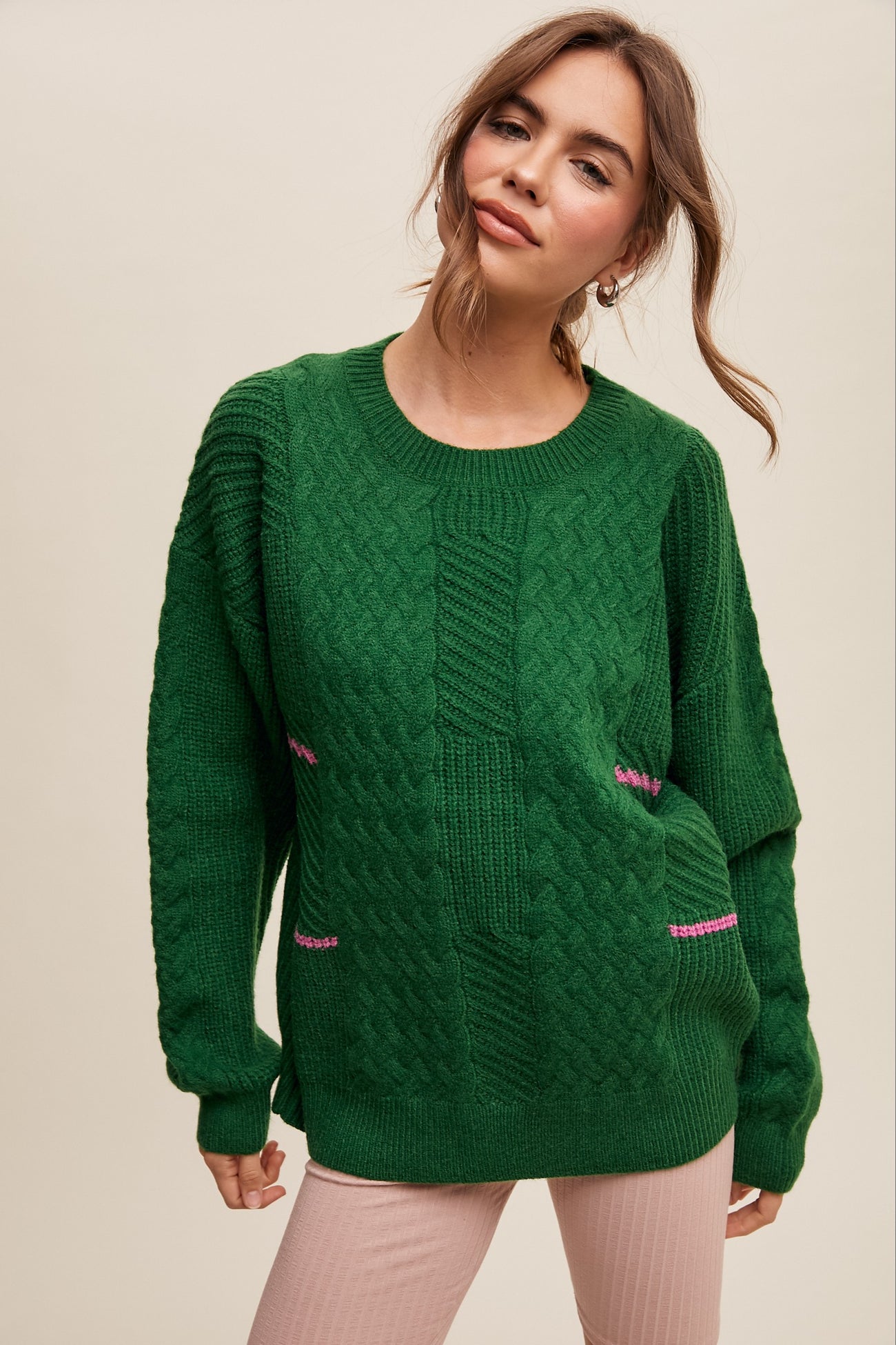 woman wearing a green cable knit sweater with contrasting pink detailing on the front