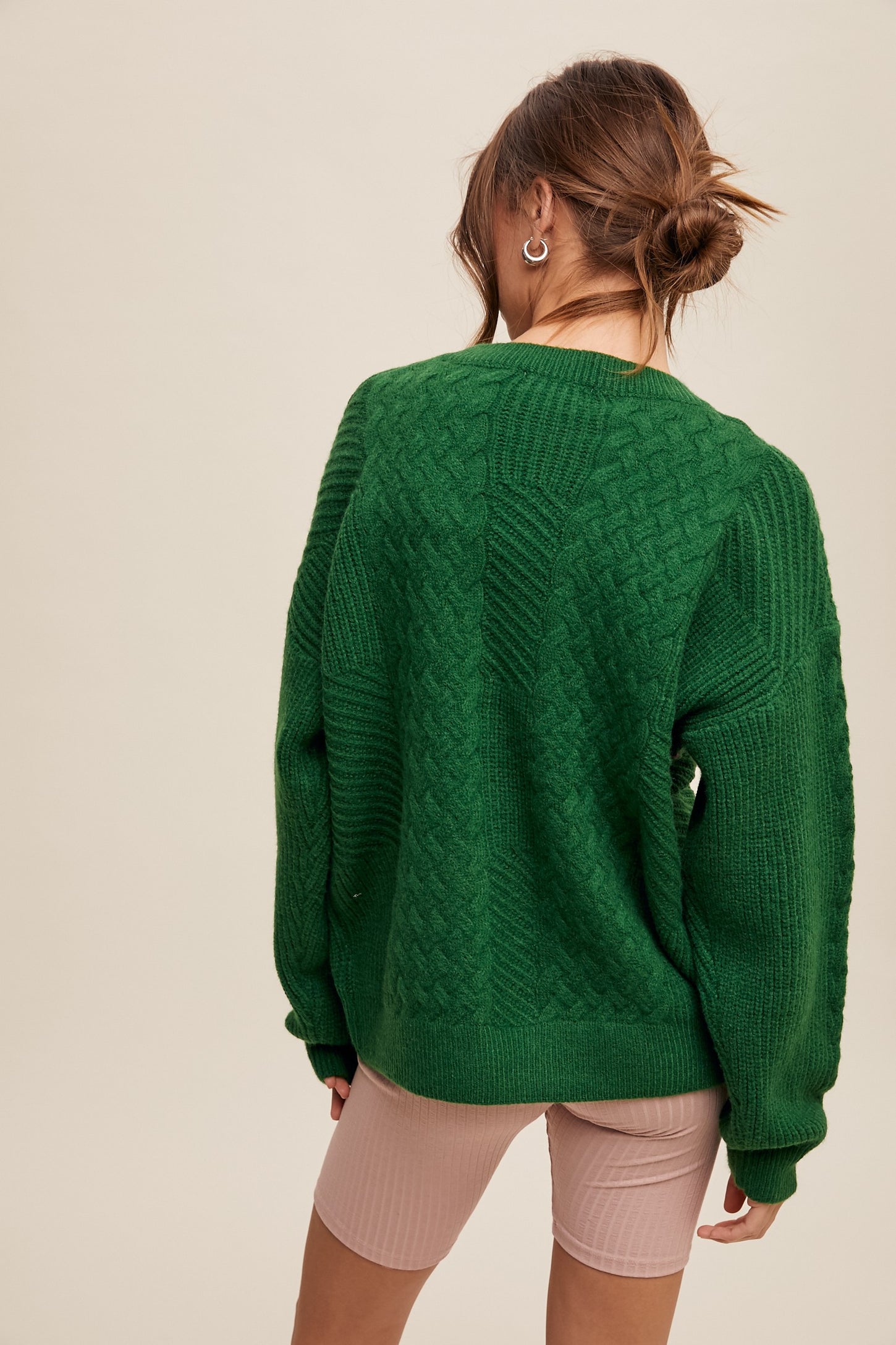 woman wearing a green cable knit oversized sweater with long sleeves, standing with her back to the camera