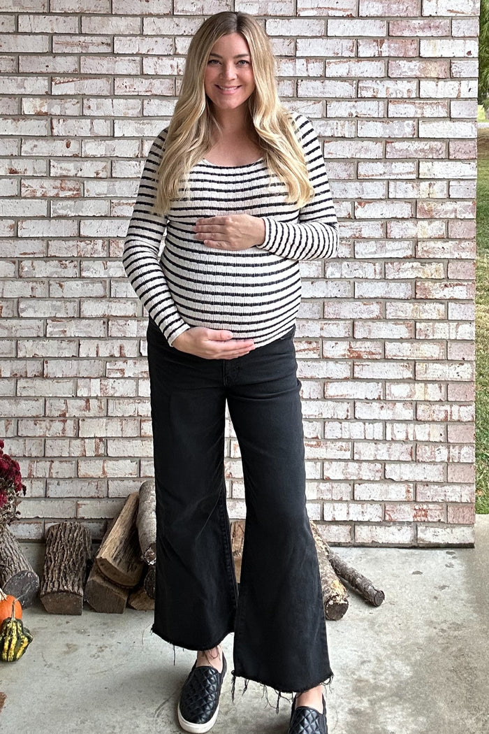 woman wearing a black and white striped maternity top and black wide-leg pants, showcasing her baby bump while standing outdoors