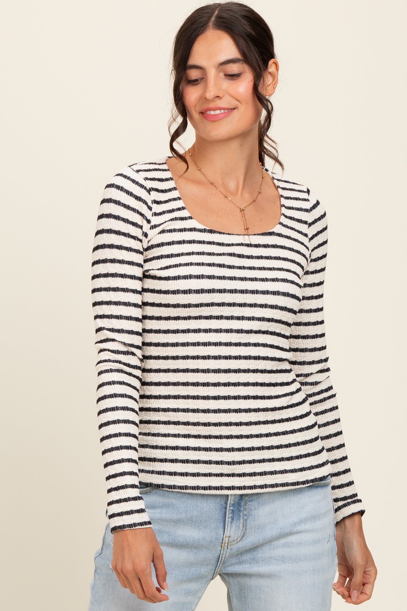 woman wearing a white and black striped long sleeve top with a square neckline and light blue jeans
