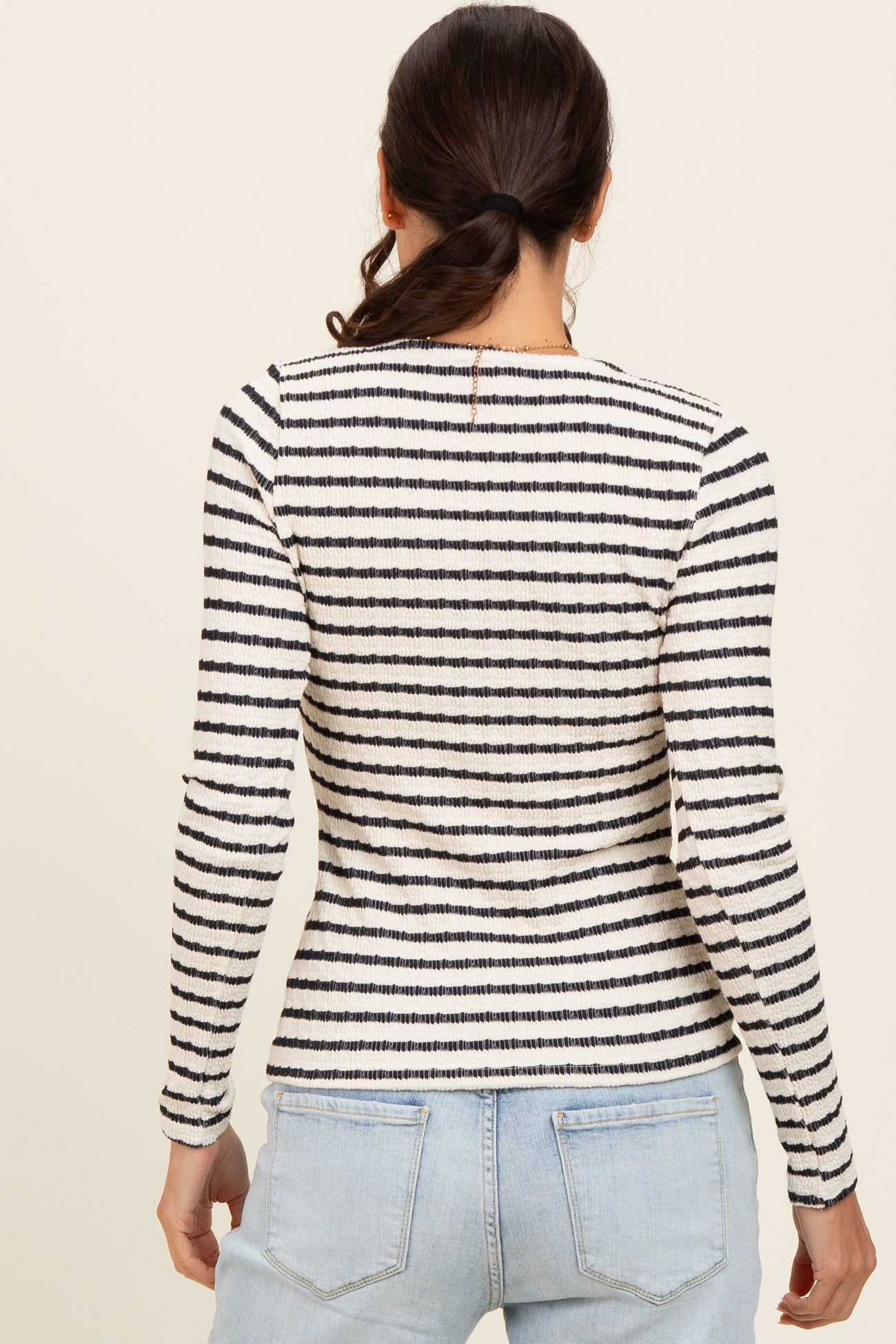 woman wearing a striped long sleeve top with a fitted silhouette and a round neckline, seen from the back