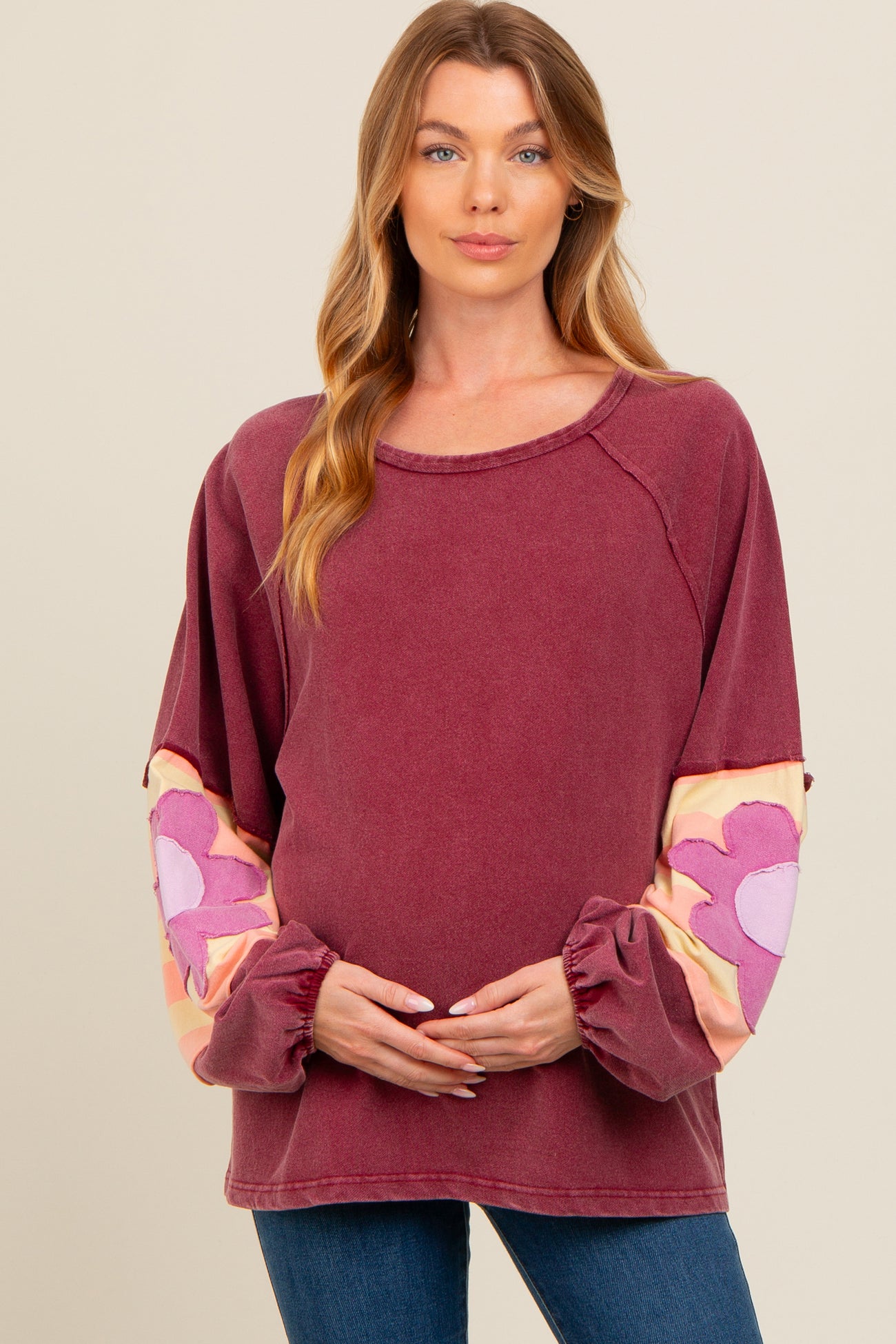 woman wearing a burgundy maternity sweatshirt with floral patterned sleeves and holding her baby bump